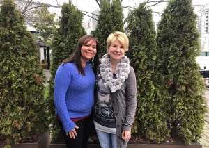 two women standing in front of some bushes smiling at the camera